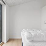 Schlafzimmer mit weißem Bett und großem Fenster zur Terrasse.