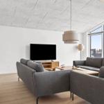 Wohnzimmer mit grauem Sofa, Fernseher und Holzmöbeln. Große Fenster und Backsteinwand.