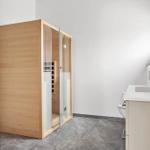 Bad mit Holzsauna, Waschbecken und Toilette. Graue Fliesen und weiße Wände.