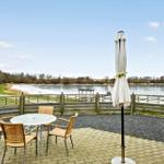 Terrace with table, chairs, and umbrella. View of a lake with shoreline path and woods.