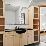 Bathroom with sink, mirror, and wooden cabinets. Corridor to the bedroom.