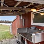 Outdoor sink at red wooden hut with view of pond and grass.
