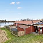 Red building by the lake with grill area and terrace.