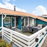 Ein Haus mit Terrasse, Tisch und Stühlen. Weiße Brüstung und roter Dachziegel.