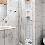 Badezimmer mit Dusche, Waschbecken und Toilette. Fliesenwand und Spiegel.