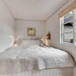 Schlafzimmer mit weißer Holzwandverkleidung, Bett und Fenster mit Blick nach draußen.