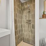 Dusche mit braunen Fliesen, Waschbecken und Toilette im Badezimmer.