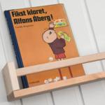 Ein Buch liegt auf einem Holzregal an einer weißen Wand.