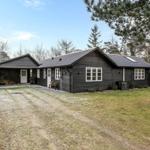 Schwarzes Holzhaus mit Garage und Rasenfläche. Umgeben von Bäumen und Hecke.