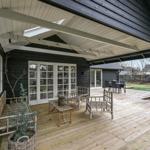 Terrasse mit Holzboden, Bänken und Tisch unter Dach. Hintergrund zeigt Garten und Haus.