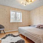 Schlafzimmer mit Holzwand, Bett, Stuhl und Fenster.