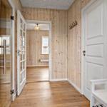 Flur mit Holzwandverkleidung, weißen Türen und Holzboden. An der Wand hängen Haken.