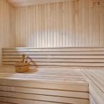 Sauna mit Holzbank und Eimer. Fenster und Holzwände sichtbar.