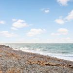 Steiniger Strand mit Wellen und blauem Himmel mit weißen Wolken.