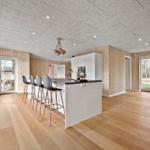 Moderne Küche mit Insel und Barhocker. Holzwände und Boden. Glastüren zu Außenbereich.