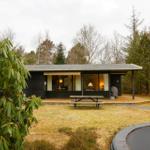 Wooden house with terrace, picnic table, and trampoline in forest area.