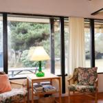 Two chairs with floral upholstery stand before large windows. A green lamp sits on a table.