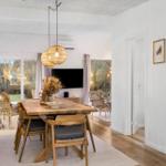 Dining room with wooden table, chairs, and wicker lamps. Corridor to kitchen and living area.