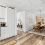 Kitchen with dining area and living room. Wooden floor, white cabinets, dining table with chairs.