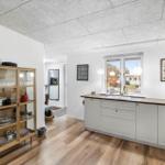 Kitchen with wooden floor, white cabinets, and glass cabinet. Window with view outside.