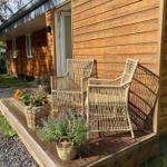 Wooden deck with two wicker chairs and flower baskets in front of a wooden house.