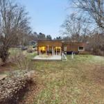 Modern wooden cabin with terrace, garden, and trees in the background.