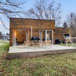Modern wooden cabin with deck, grill, and soccer goal in the yard.