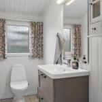 Badezimmer mit Toilette, Waschbecken und Spiegel. Fenster mit Vorhängen.