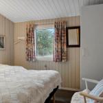 Schlafzimmer mit Bett, Fenster und Stuhl. Wandverkleidung und Vorhänge.
