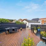 Deck with wooden planks, garden furniture, and plants. View of neighboring houses.