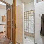 Bathroom with shower and adjacent kitchen with wooden doors.