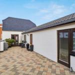 Backyard with terrace, garden furniture, and plants. White wall, brown windows, and roof tiles.