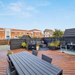 Deck with wooden flooring, seating area, and plants. View of residential buildings in the background.