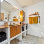 Bathroom with wooden sink counter, mirror, and toilet. Yellow towels hang on the wall.