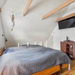 Bedroom with sloped ceiling, bed, TV, and wooden furniture.