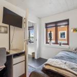 Bedroom with bed, TV, and window overlooking a house.