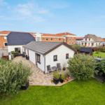 White house with terrace and garden. Surrounded by greenery and neighboring houses.
