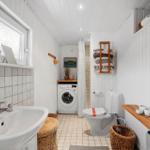 Bathroom with washing machine, toilet, and shower. Wooden shelves and baskets.