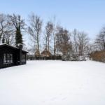 Black house on snow-covered ground with trees in the background.