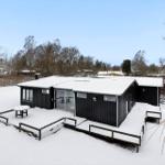 Black house with snow-covered roof and terrace in winter.
