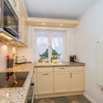 Küche mit Dunstabzug, Herd und Fenster mit weißen Vorhängen.