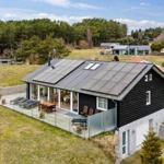 Schwarzes Haus mit Terrasse und Solarpanel auf grünem Grundstück.