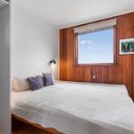 Schlafzimmer mit Bett, Fenster und Holzwand. Kleine Nachttischlampe und Bild an der Wand.