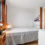 Schlafzimmer mit Bett, Fenster und Regal. Holzwände und weißer Schrank.