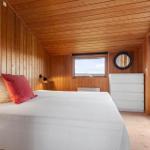 Schlafzimmer mit Holzwand, Bett, Schrank und Fensterblick auf Wasser