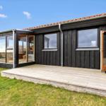 Holzhaus mit Terrasse und Glasveranda. Tür offen. Grasfläche vor dem Haus.