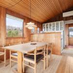 Esszimmer mit Holztisch, Stühlen und Küchenbereich. Holzwände und -decke.