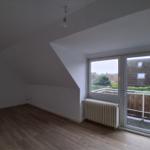 Zimmer mit Holzboden und Balkontür. Dachneigung und Heizkörper sichtbar.