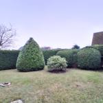 Garten mit Rasenfläche und gestutzten Hecken sowie Bäumen.