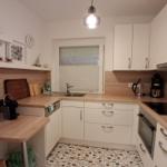 Küche mit weißen Schränken, Holzoberflächen und Mosaikboden.